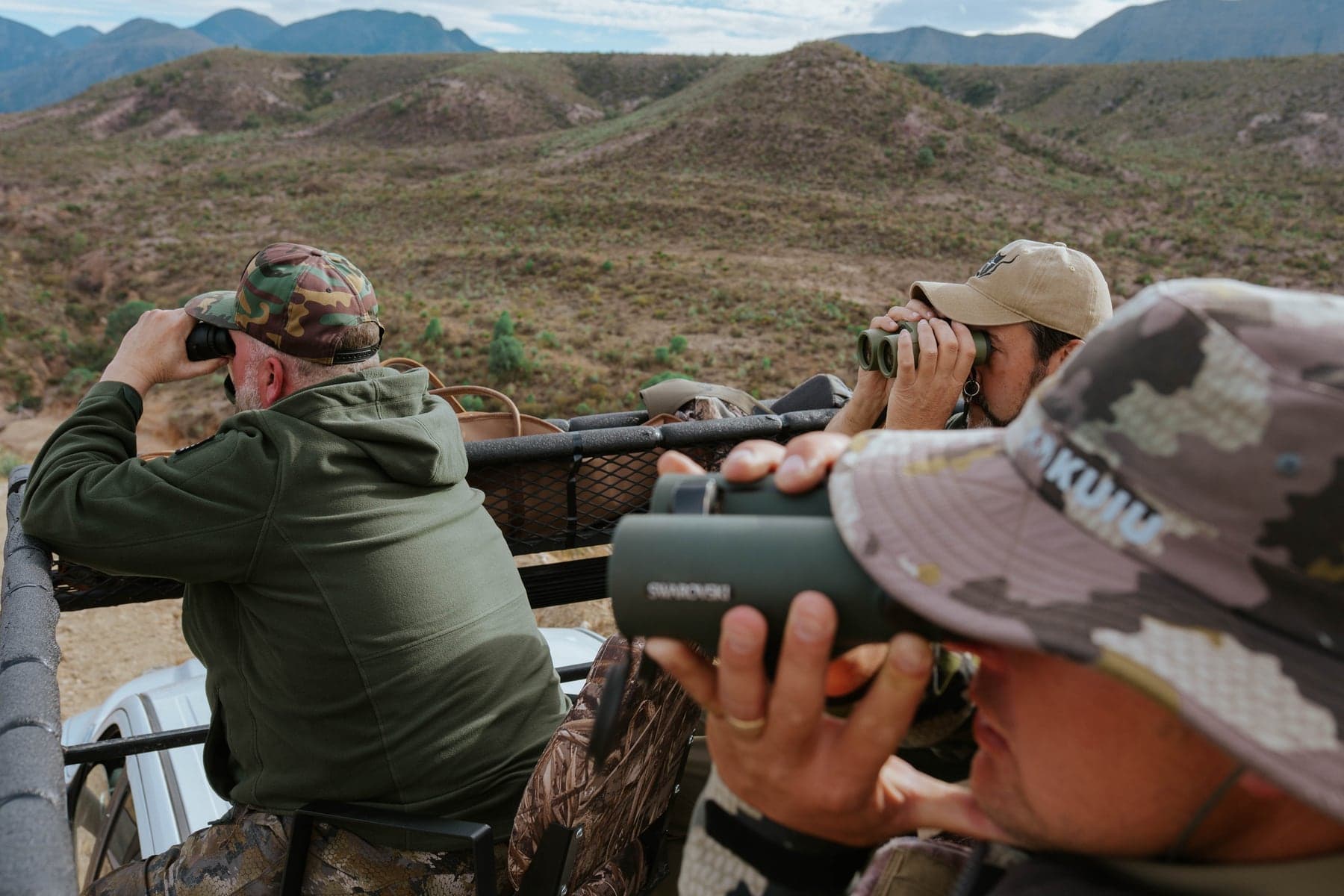 Three hunters glassing through binoculars from a high-rack truck over the Coahuila hills