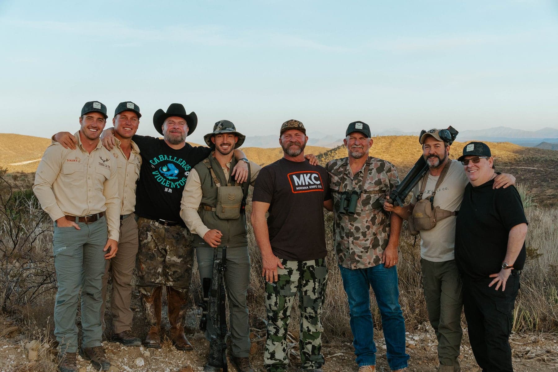 Eight hunters and guides standing arm-in-arm on a Coahuila ridge at golden hour